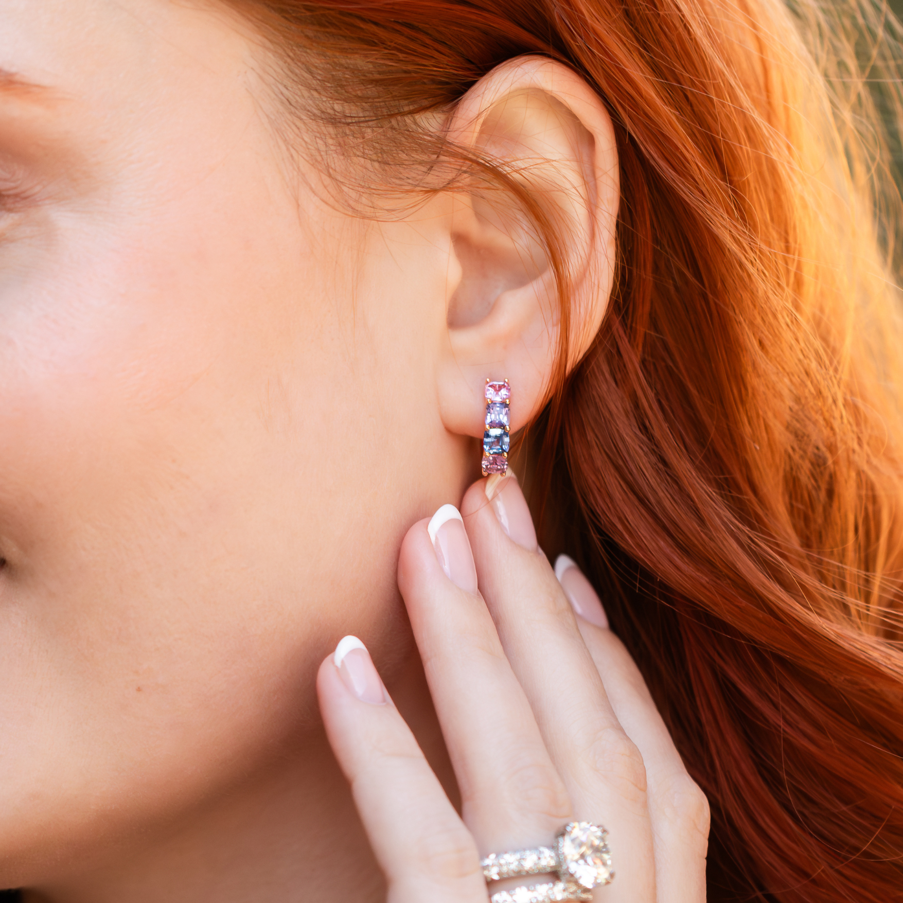 woman wearing diamond ring and band and multi-color stone huggie earring