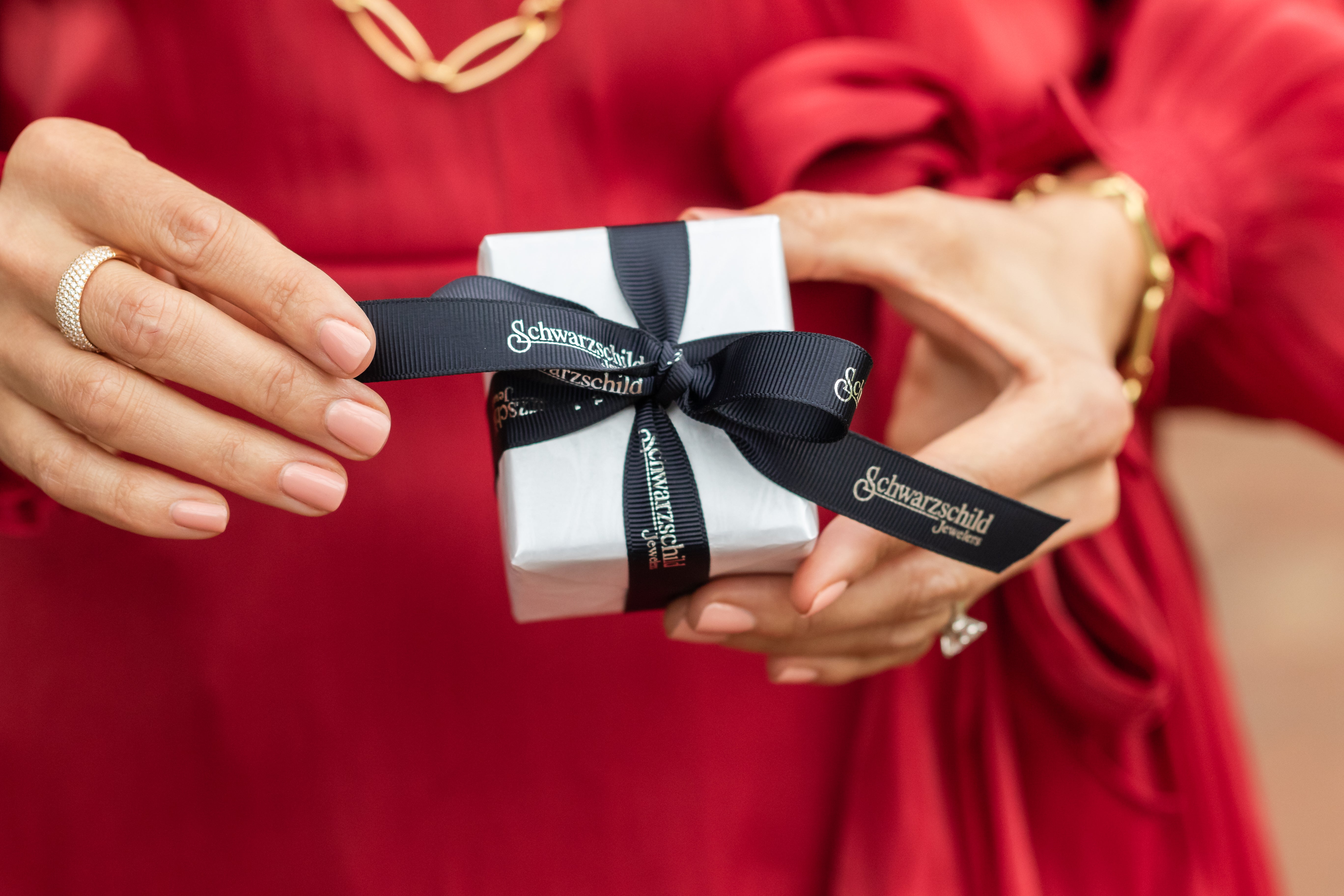 A woman gently unwrapping a gift and holding an open jewelry box, revealing a sparkling piece of jewelry inside.