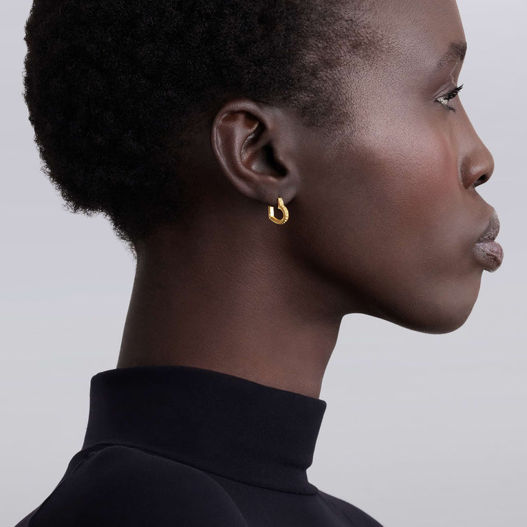 Profile of a woman wearing gold hoop earrings against a neutral background