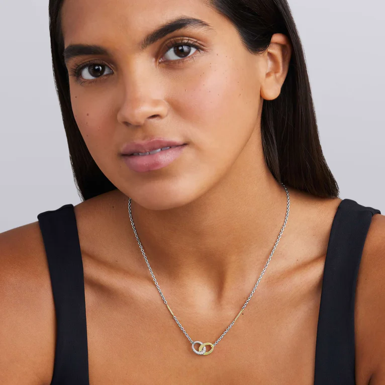 Woman wearing a silver necklace with a black top against a neutral background