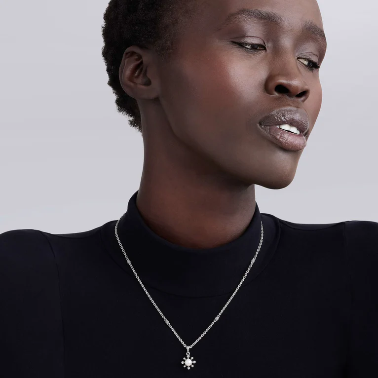 Woman wearing a silver necklace with a pendant against a plain background