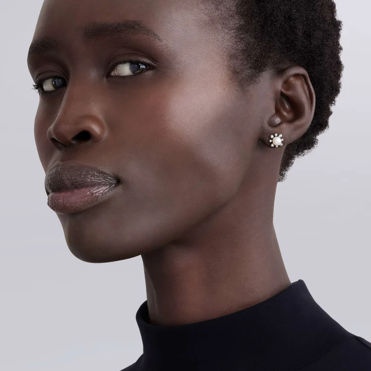Close-up of a woman wearing a black turtleneck and earrings against a plain background