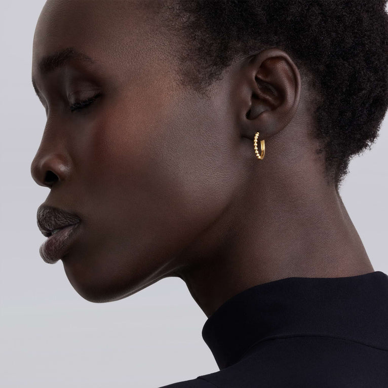 Profile of a person wearing a gold hoop earring against a neutral background